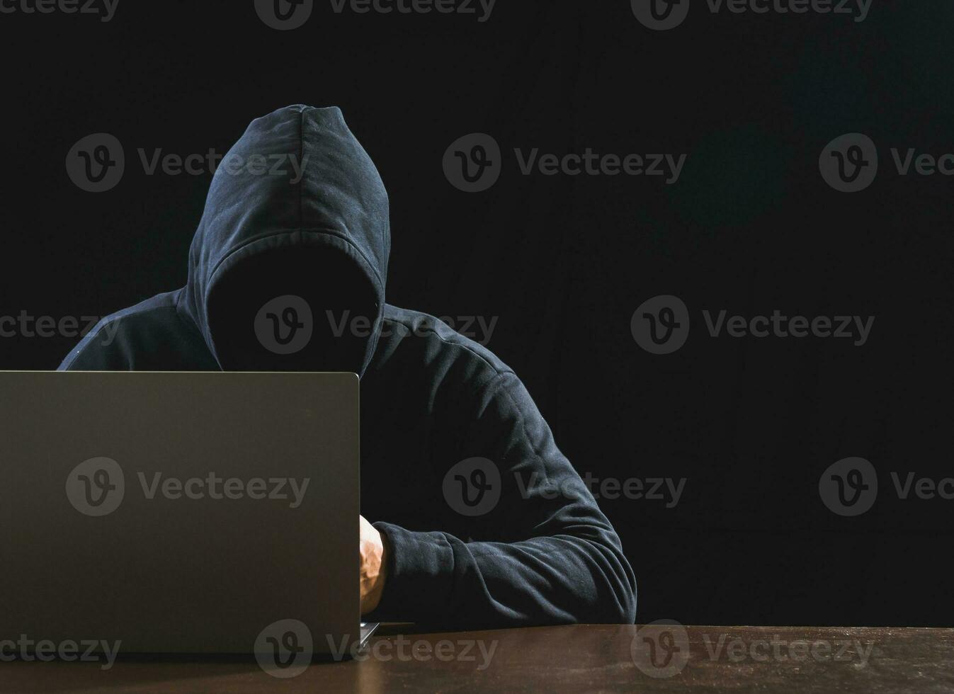 Hacker spy man one person in black hoodie sitting on a table looking computer laptop used login password attack security to circulate data digital in internet network system, night dark background. photo