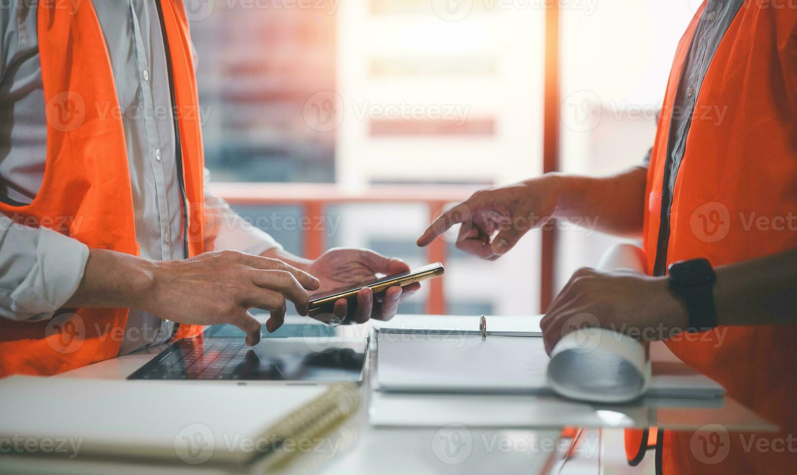 engineers or foreman workers discussion project using smartphone and wearing safety shirt on work site photo