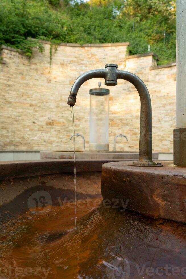 Bebiendo agua vierte desde el grifo en el calle. un antiguo oxidado grifo desde cuales agua carreras dentro un agua tanque foto