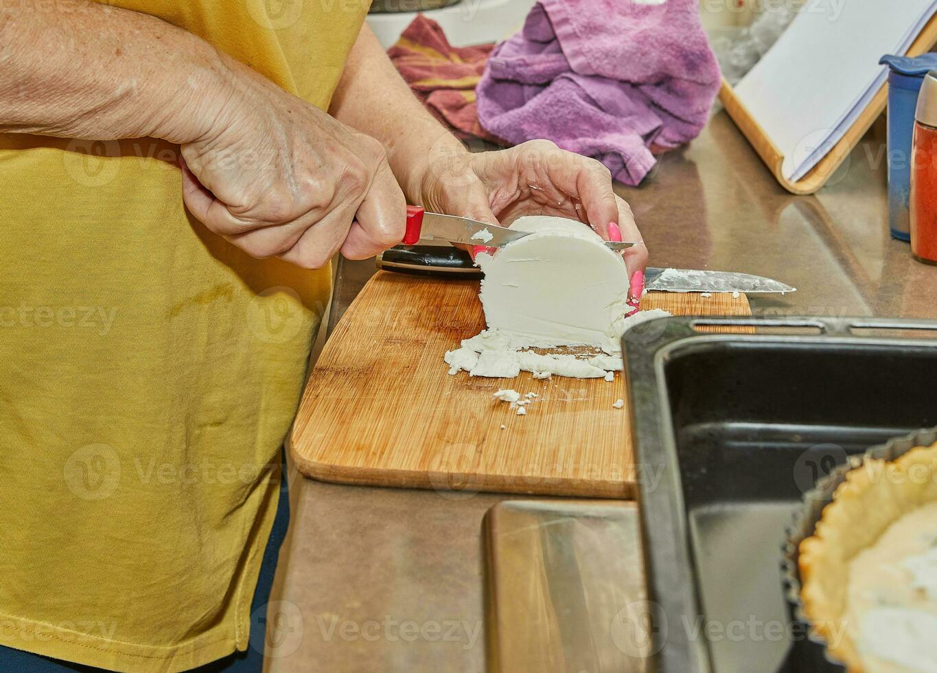 Chef cuts the cheese with knife on wooden board for making a pie photo