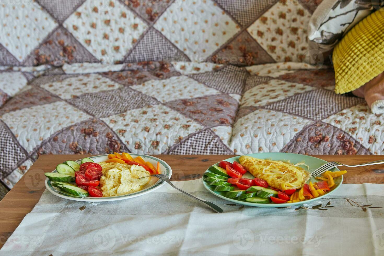 Mañana sano desayuno de revuelto huevos con parmesano queso, pepinos, Cereza Tomates y dulce pimientos en el café mesa en frente de el sofá foto