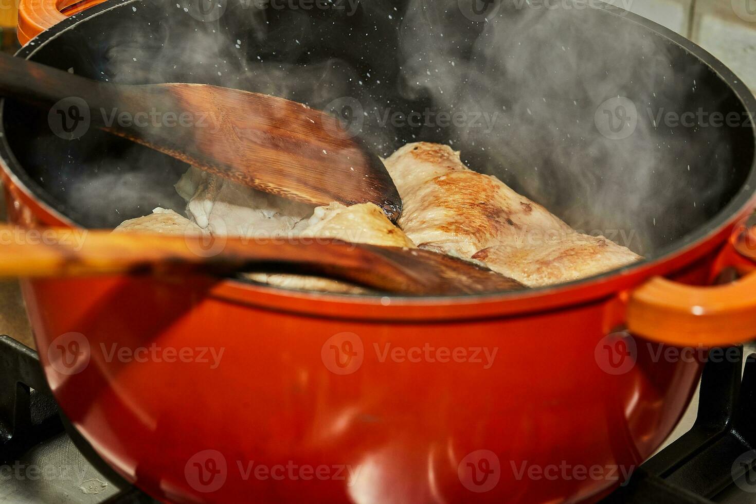 Chicken legs are fried in pan, wooden sticks for stirring and steam photo