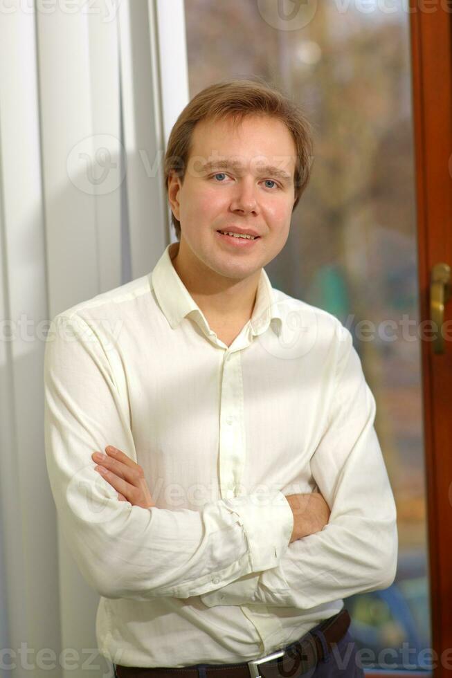 Happy young man standing by the window with blinds photo