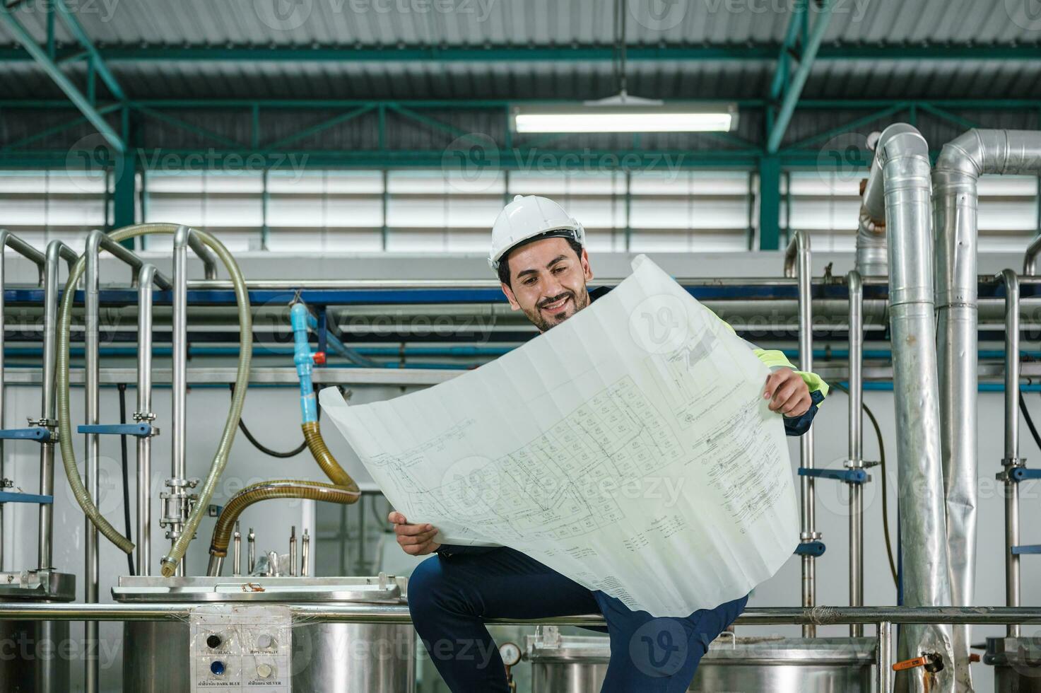 Caucasian technician engineer man sitting and holding blueprint of industrial project with boiler and pipeline in beverage processing plant photo