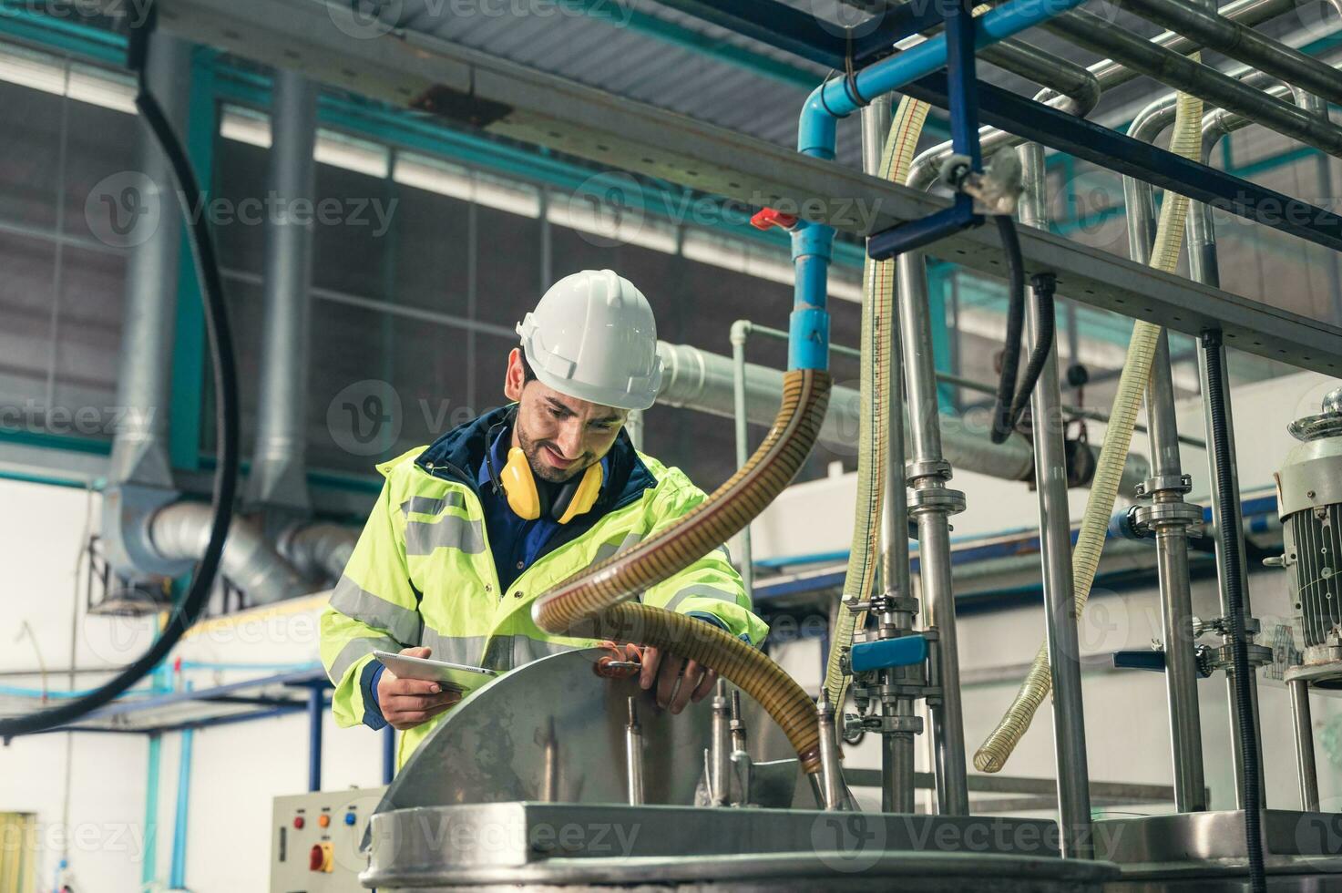 Caucasian technician engineer man in uniform with tablet checking and control boiler tanks and liquid pipeline in production line at factory photo