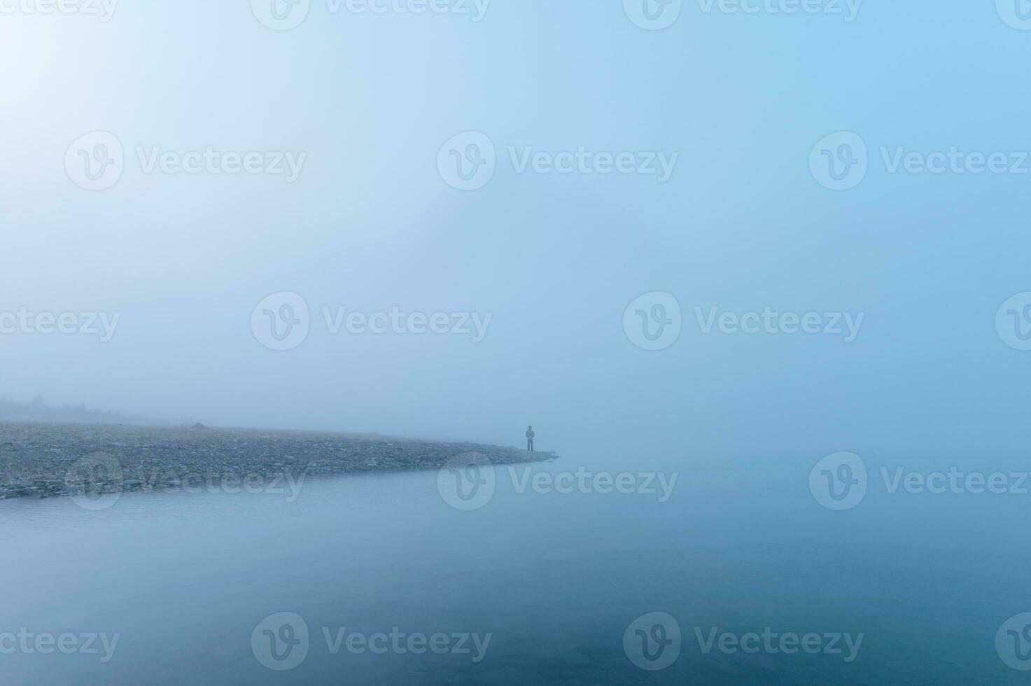 Traveler man standing alone in blue fog with rocky mountains by the lake in the morning photo