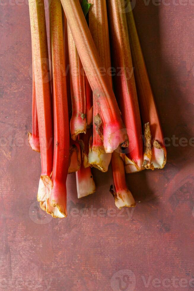 Fresh ripe green and red rhubarbs on a rustic burgundy table 3 photo