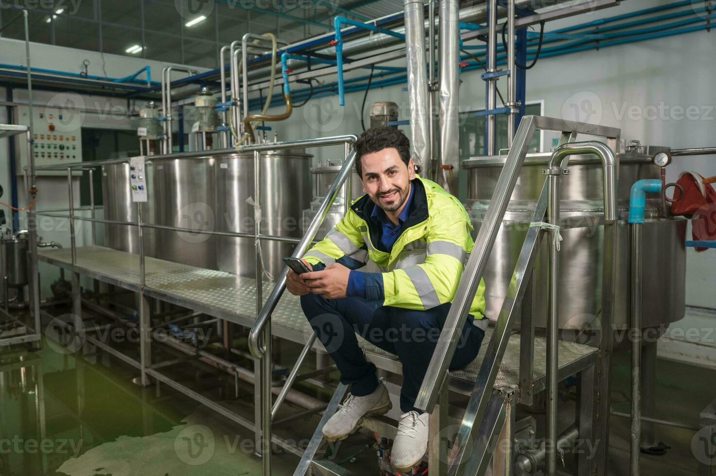 Caucasian engineer man using smartphone during break time on stair at processing plant photo