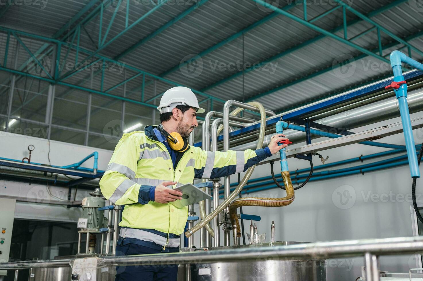 Caucasian technician engineer man in uniform with tablet checking and control boiler tanks and liquid pipeline in production line at factory photo