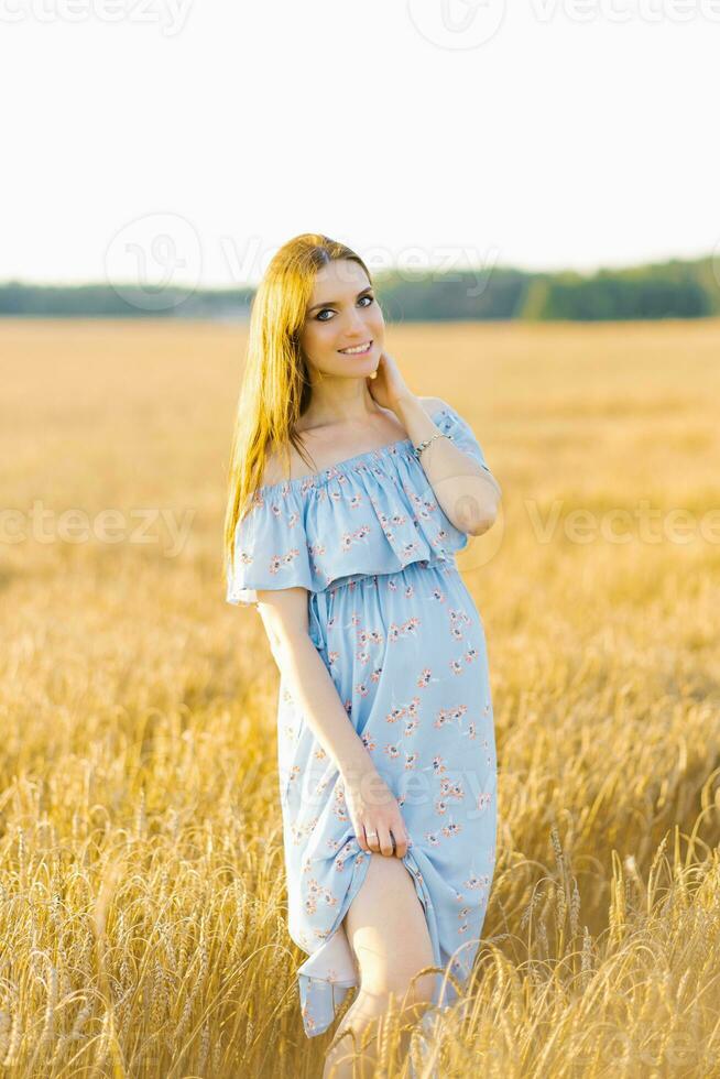 Young pregnant woman in blue dress relaxing outside in nature photo