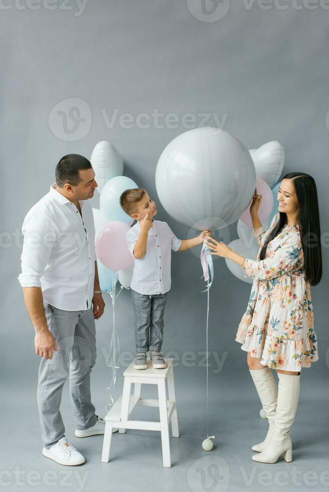 Gender reveal party. Stylish beautiful family with a baby pop a balloon to find out the gender of the unborn child in the family photo