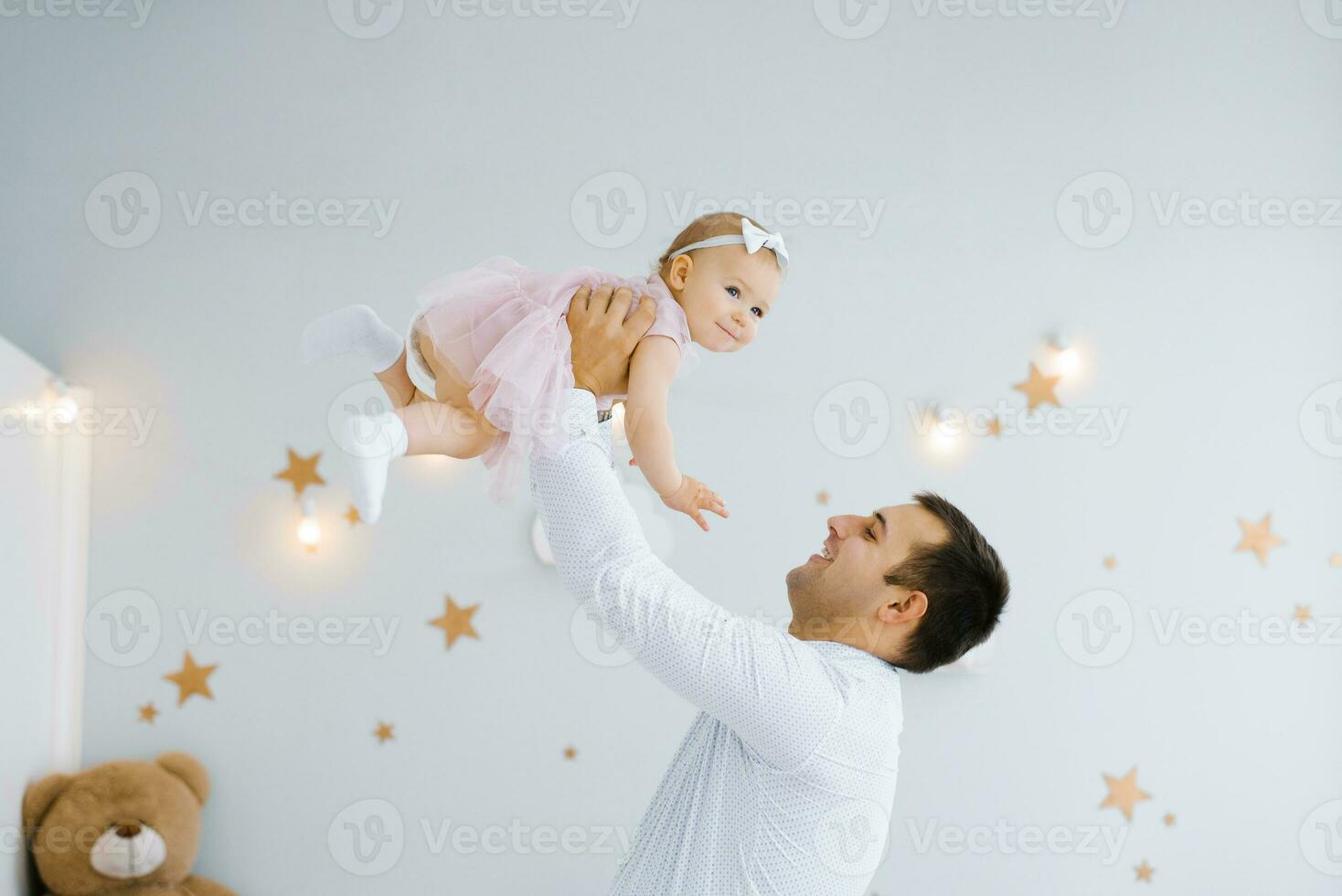 padre levantamiento bebé muchacha. contento padre escoge arriba y lanza su levantamiento un pequeño niño. hogar atmósfera, contento familia riendo bebé foto