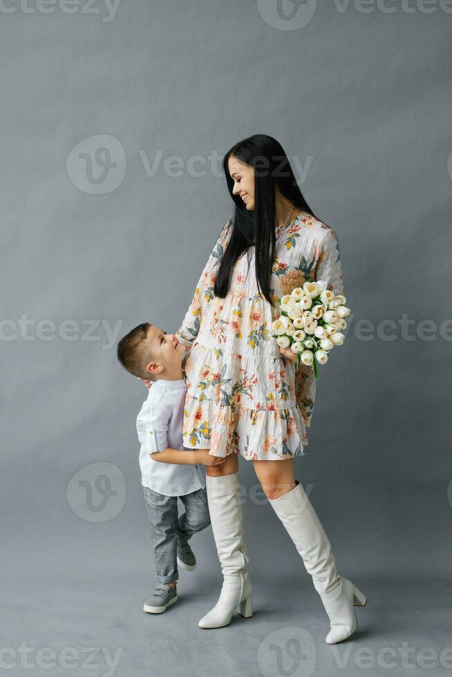 Portrait of a young mother with a small child standing on a gray background, family love and sincerity photo