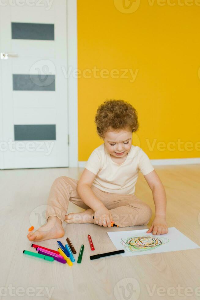 linda pequeño chico es sentado a hogar en el piso y dibujo un dibujo con de colores Lápices niño desarrollo y creatividad para preescolares y primario colegio niños en jardín de infancia o a hogar foto