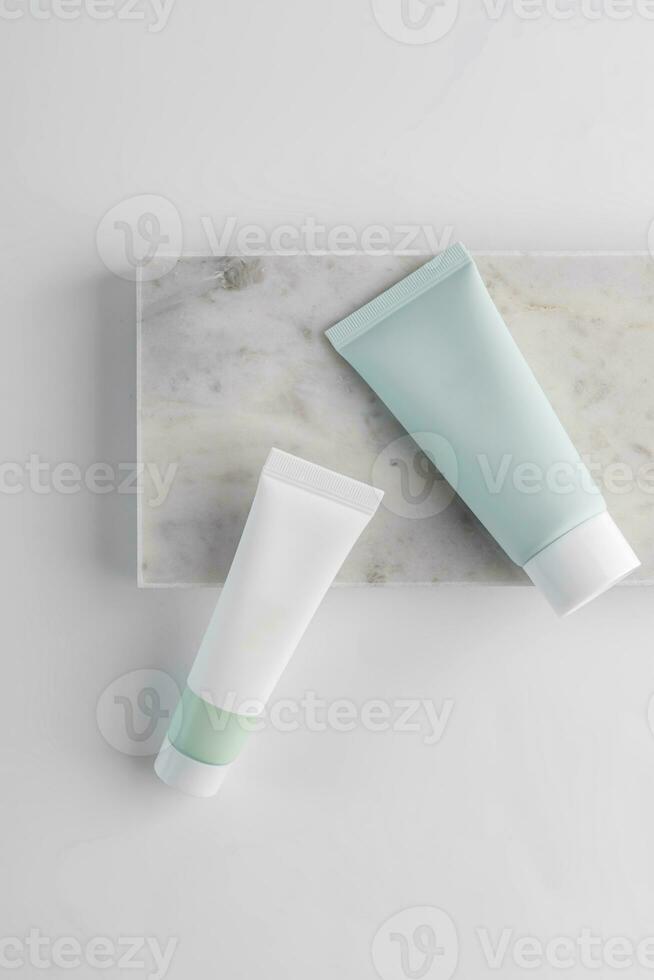 blanco y verde cosmético tubos en un blanco antecedentes en mármol bandeja. el concepto de un crema con natural ingrediente y no pruebas en animales foto
