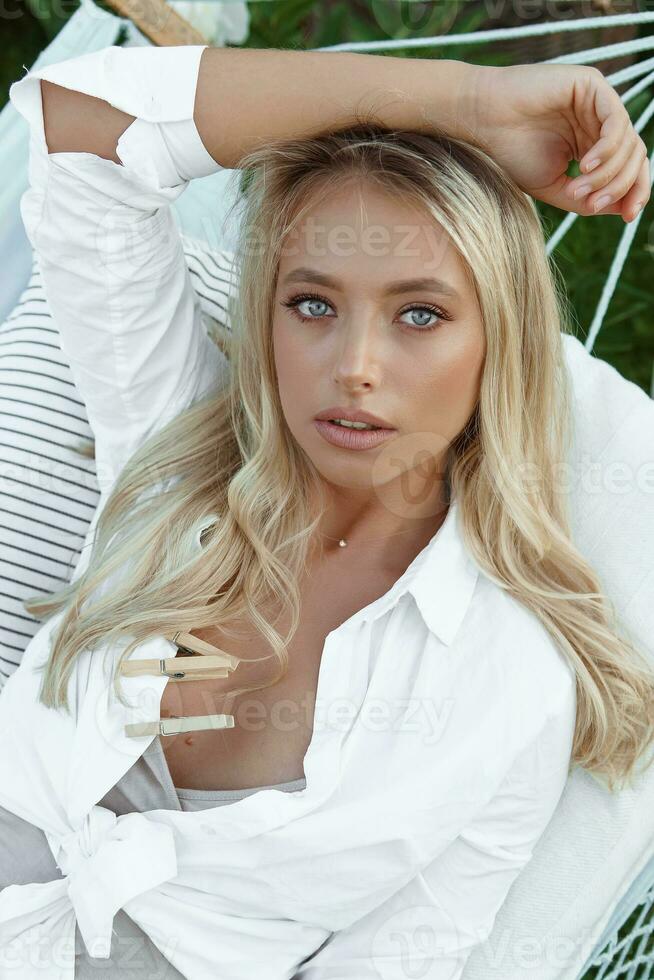 A beautiful blonde woman is lying on a hammock in her summer cottage. The concept of life in the country and summer holidays. photo