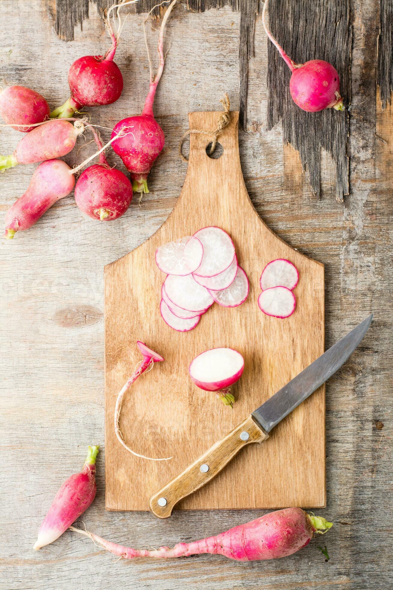 Fresh chopped radishes and a knife on a cutting board on a wooden