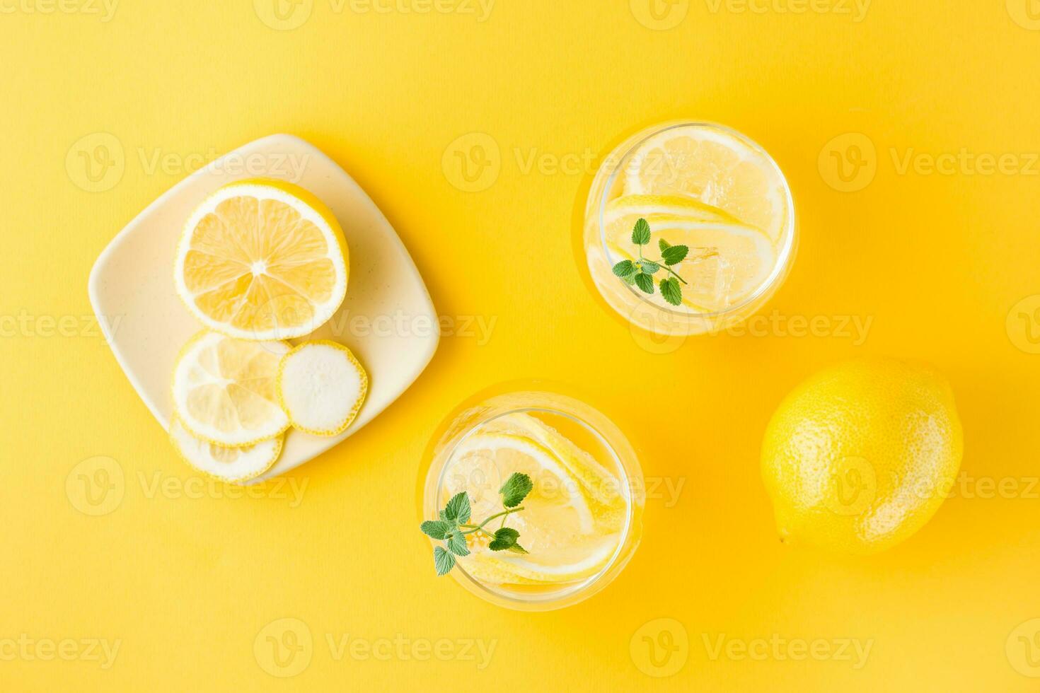 Sparkling water with lemon, melissa and ice in glasses and lemon slices on a saucer on a yellow background. Alcoholic drink hard seltzer. Top view photo