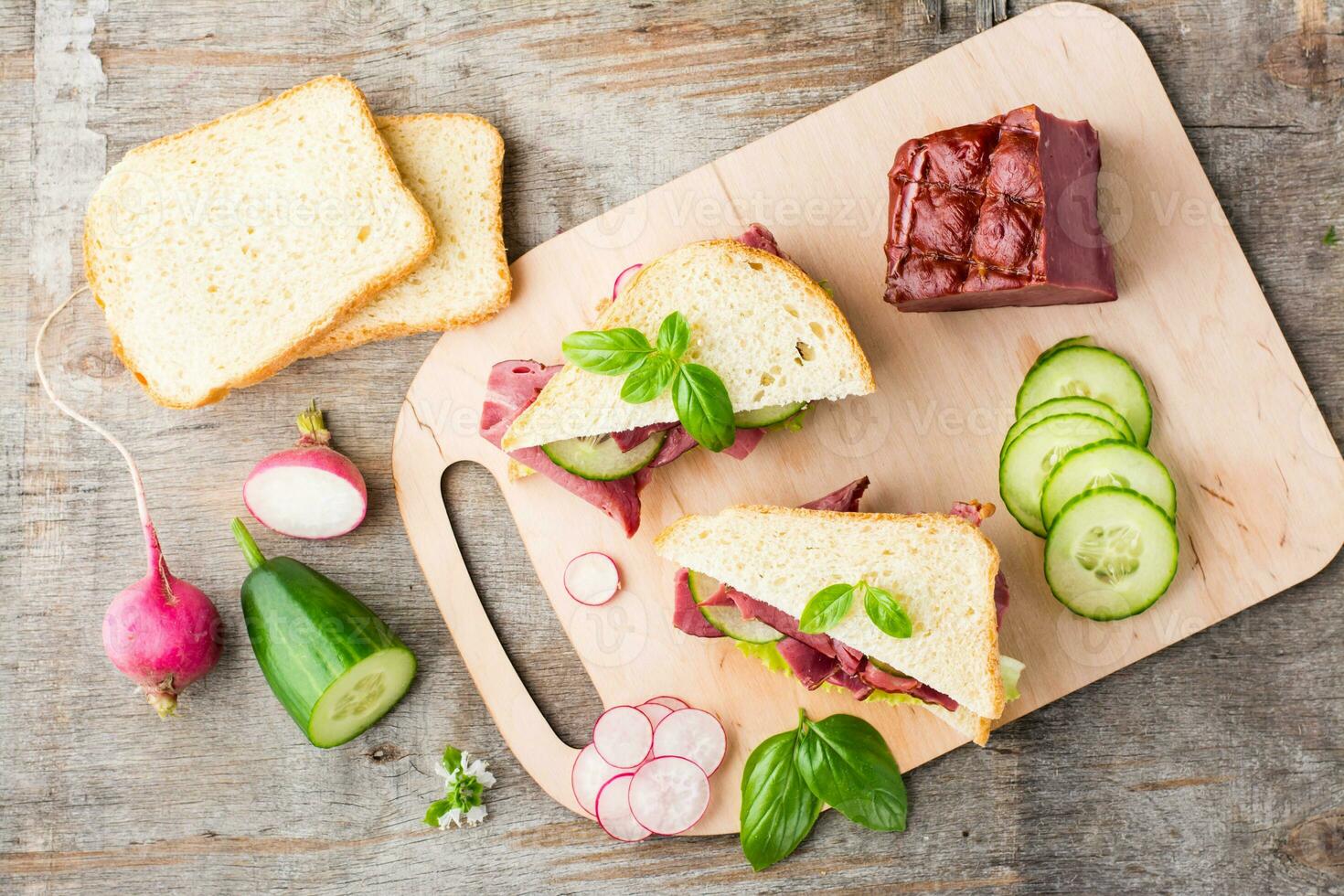 Fresh sandwiches with pastrami, cucumber and radish on a cutting board. American snack. Rustic style. Vertical view. Top view photo