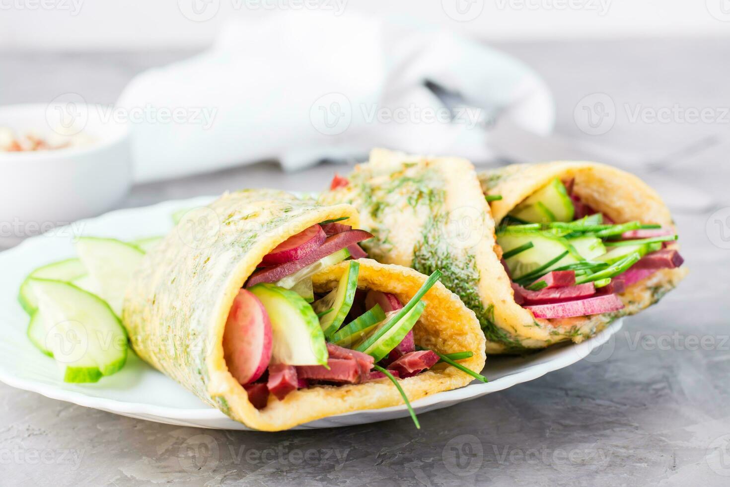 Egg rolls filled with pastrami, cucumber, radish and green onions on a plate on the table. Hearty and high-calorie snack photo
