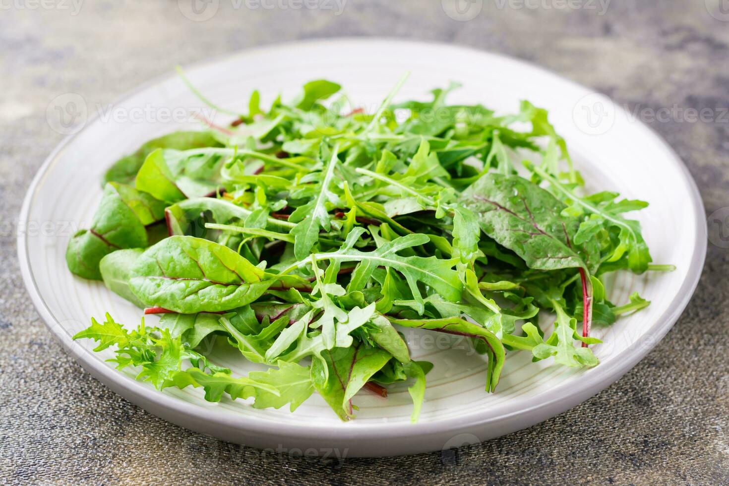 A mixture of fresh arugula, chard and mizun leaves on a plate  on the table. Vegetarianism, healthy eating. Close-up photo