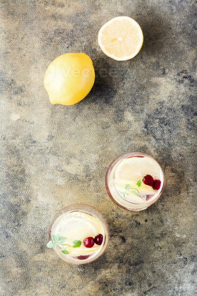 Summer refreshing cold cocktail with lemon, lemon balm and cherry - hard seltzer in glasses on the table .  Top and vertical view. Copy space photo