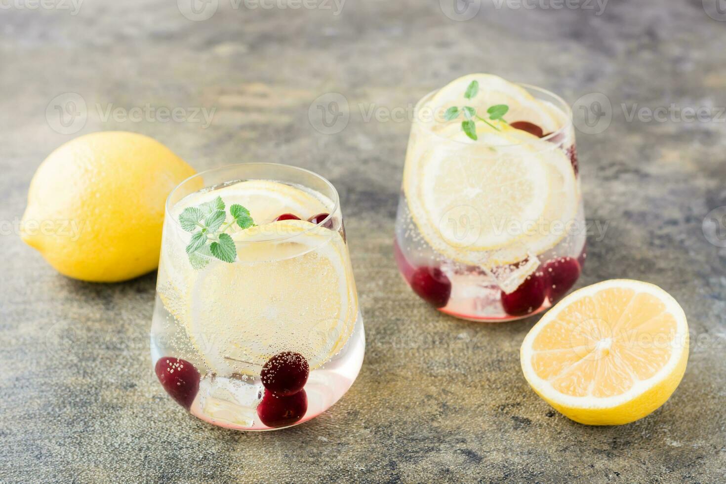 Summer refreshing cold cocktail with lemon, lemon balm and cherry - hard seltzer in glasses on the table photo