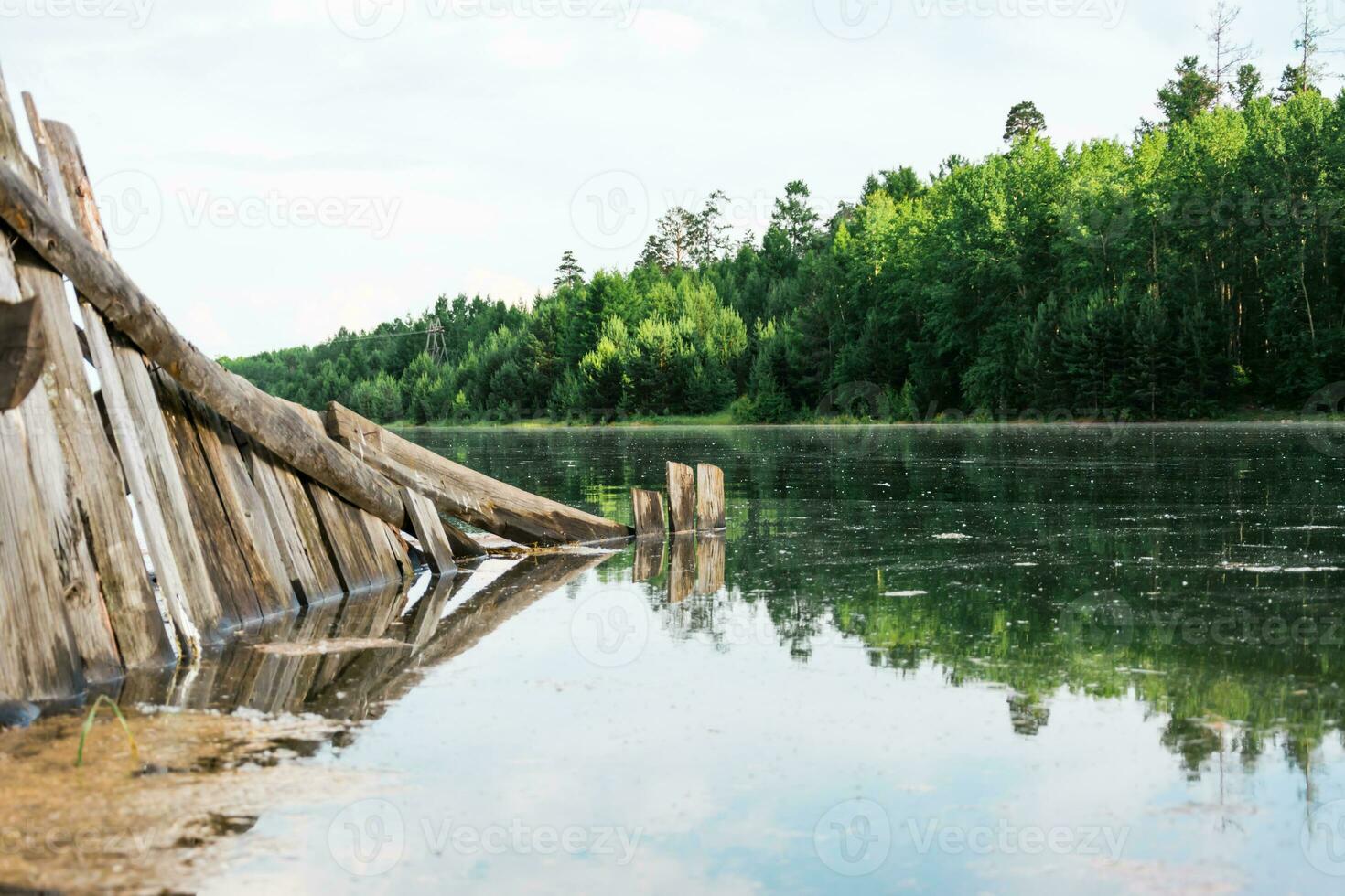 An old broken wooden fence is flooded by a flood on the river bank. Natural disaster and destruction. Beautiful landscape. photo