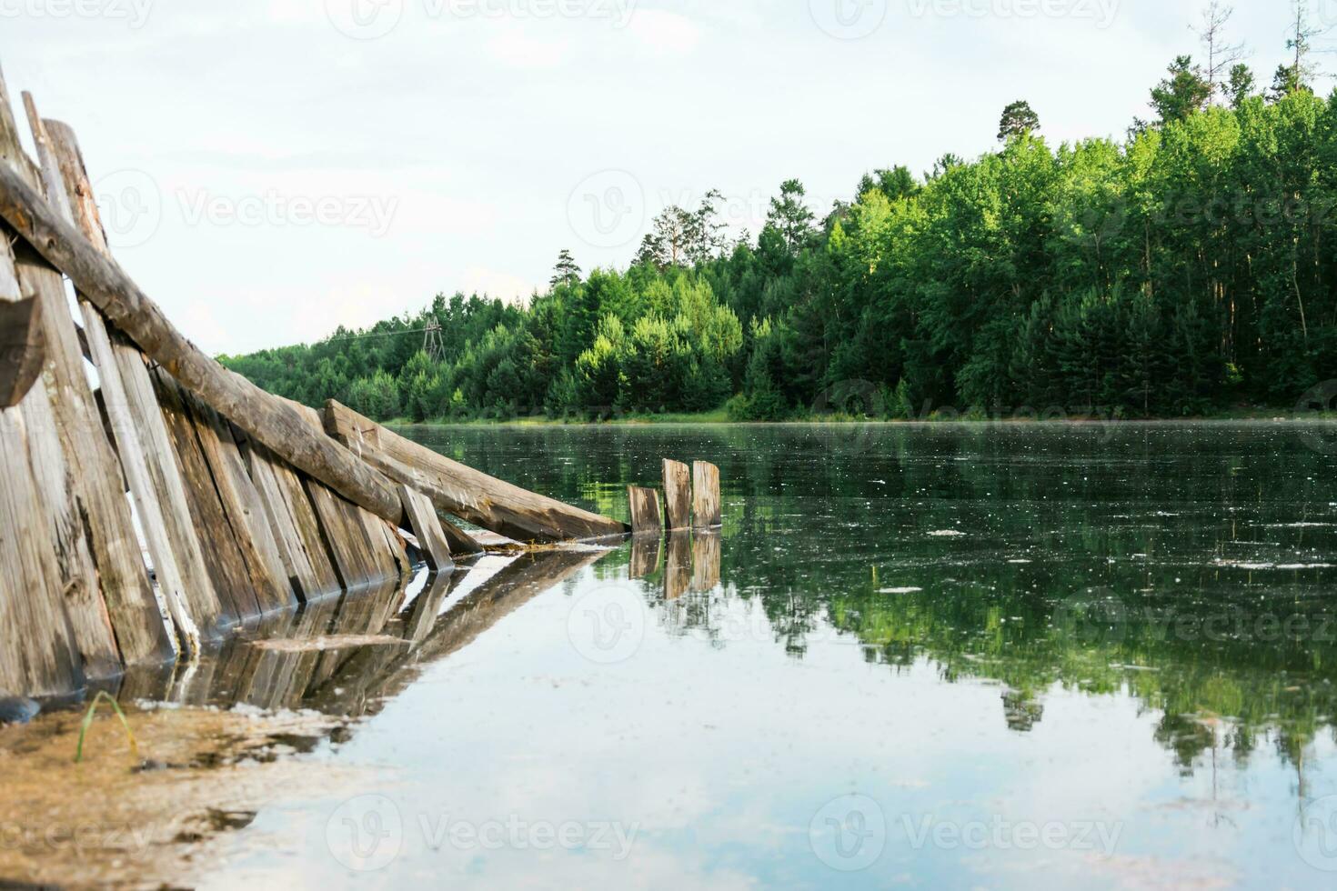 An old broken wooden fence is flooded by a flood on the river bank. Natural disaster and destruction. Beautiful landscape. photo