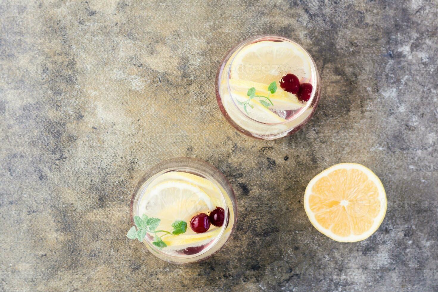 Summer refreshing cold cocktail with lemon, lemon balm and cherry - hard seltzer in glasses on the table .  Top view photo