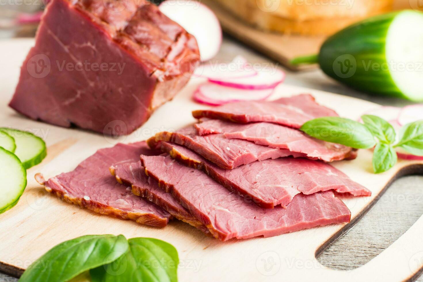 Fresh sliced marbled beef pastrami and vegetables on a cutting board. American delicacy. Rustic style. Close-up photo
