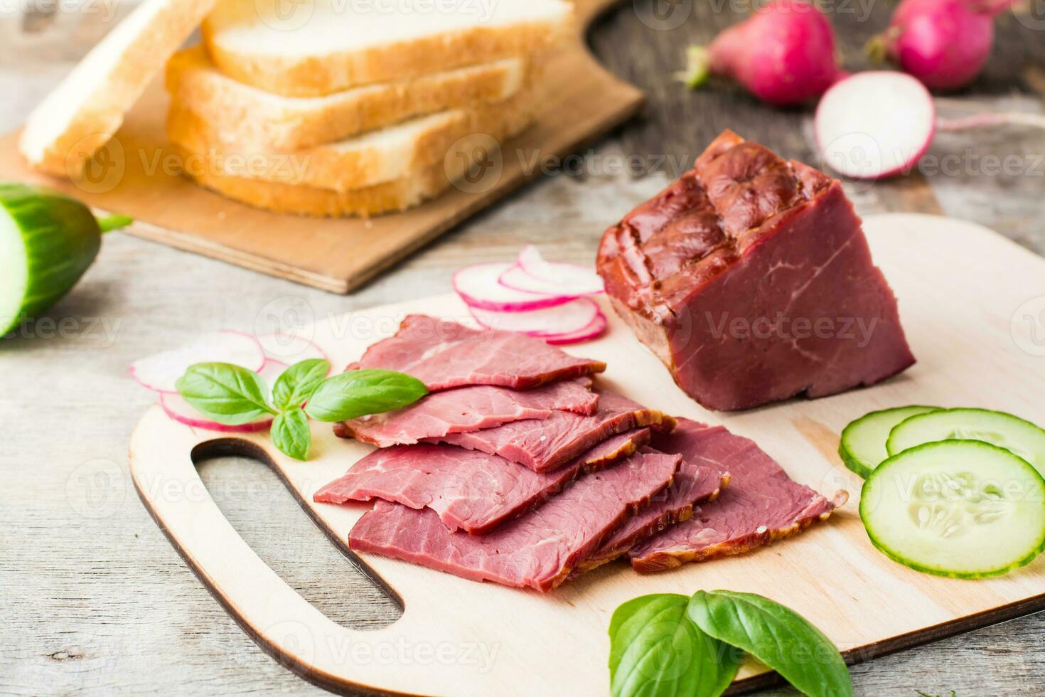 Fresh sliced marbled beef pastrami and vegetables on a cutting board. American delicacy. Rustic style photo