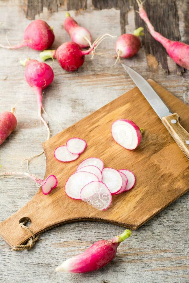 Fresh chopped radishes and a knife on a cutting board on a wooden table. Vegetables for a vegetarian diet. Rustic style. Vertical view photo