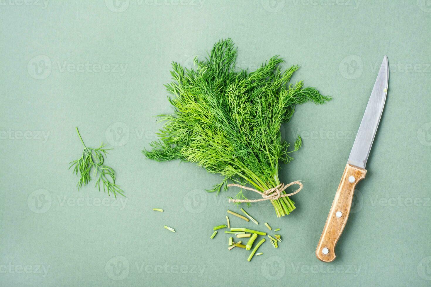 A knife cuts off the stems from a bunch of fresh dill on a green background. Vitamin greens in a healthy diet. Top view photo