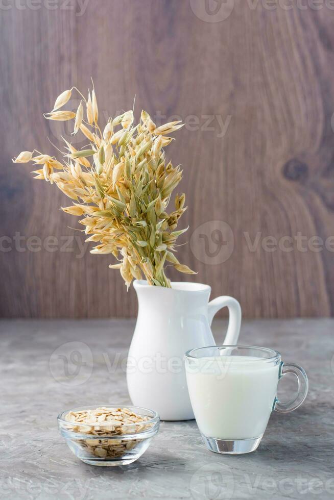 avena Leche en un taza, harina de avena y orejas de maíz en un jarra en el mesa. alternativa a de vaca leche. sano dietético no alergénico alimento. vertical ver foto