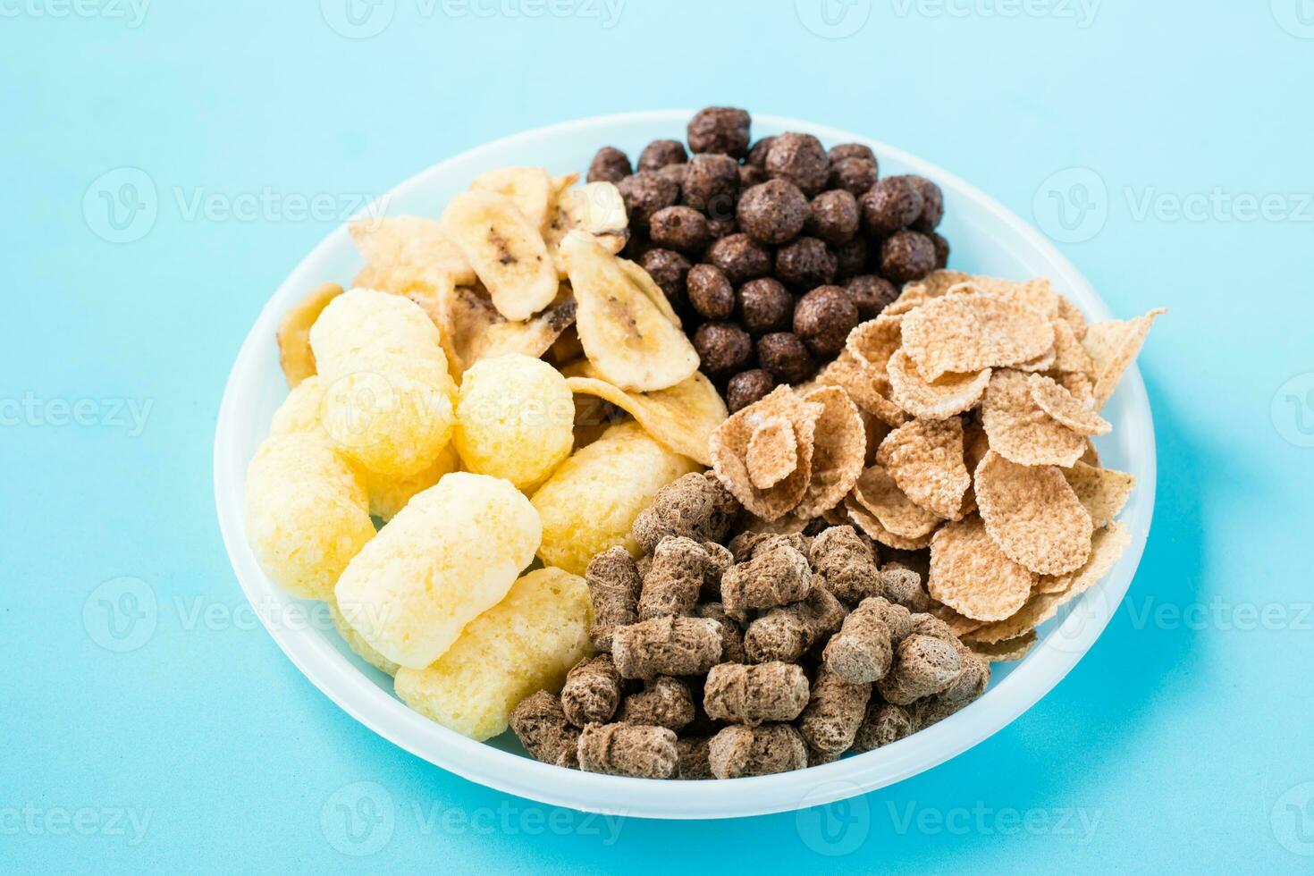 A plate with different types of breakfasts and snacks oatmeal, cereal, chocolate balls, banana chips and rye bran on a blue background photo
