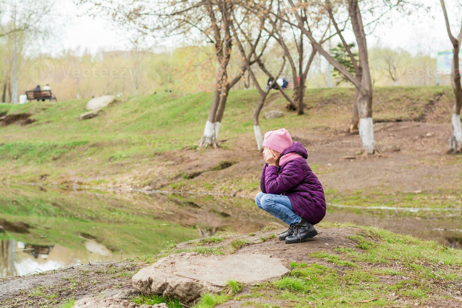 A lonely girl sits and cries covering her face with her hands on the lake in the park. Mental health photo