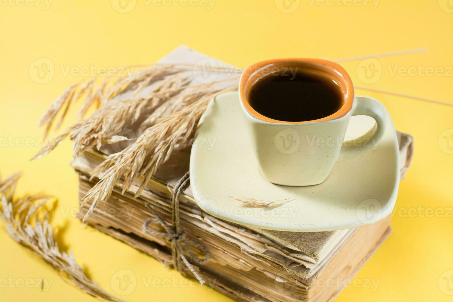 A cup of coffee on old books and dry ears of corn in yellow and harsh light. Wellness, harmony, inclusiveness photo