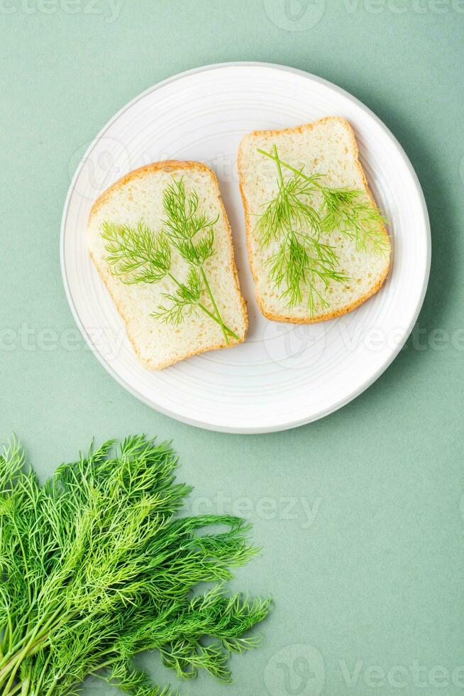 Sandwiches of white bread and fresh dill on a plate and a bunch of dill on a green background. Vitamin Herbs in a healthy diet. Top and vertical view photo