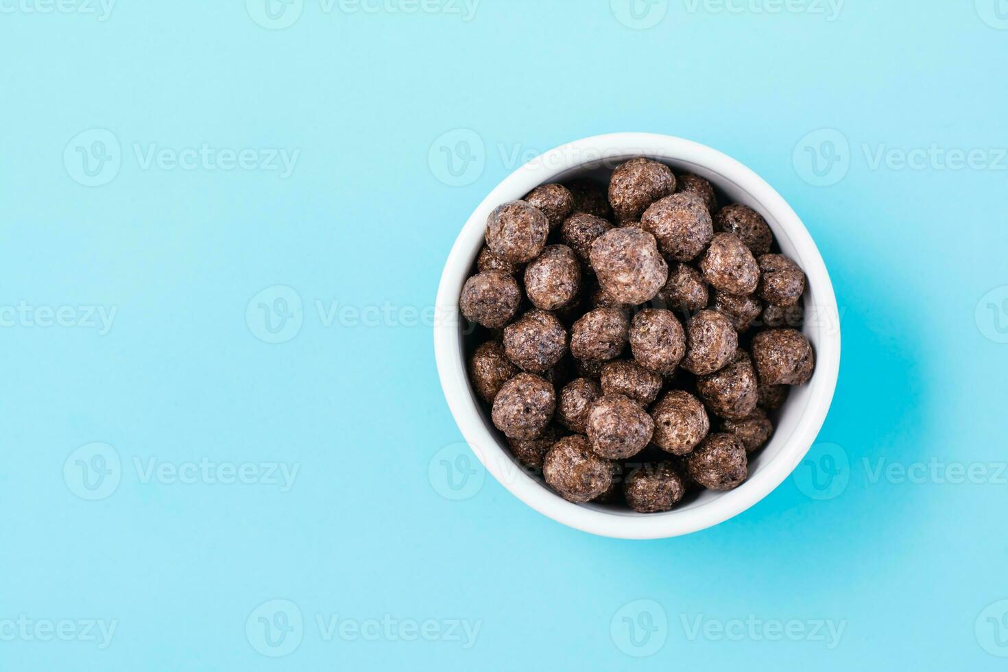 A bowl with cereal chocolate balls dry breakfast on a light blue background. Top view photo