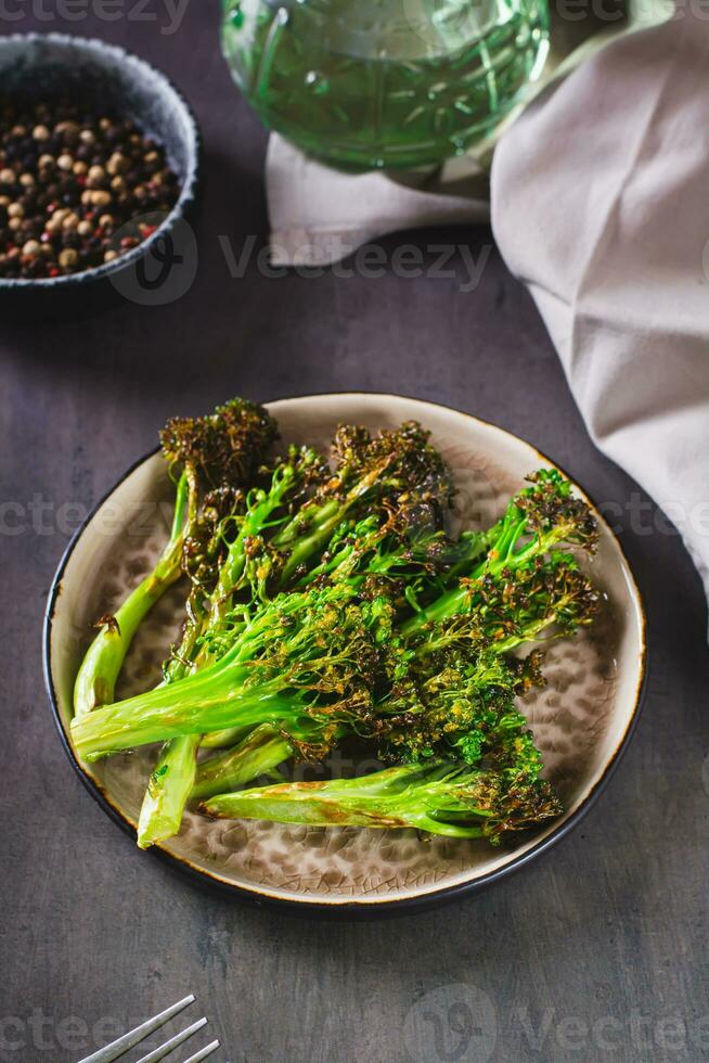 Roasted fresh broccoli sprouts in oil on a plate on the table vertical view photo