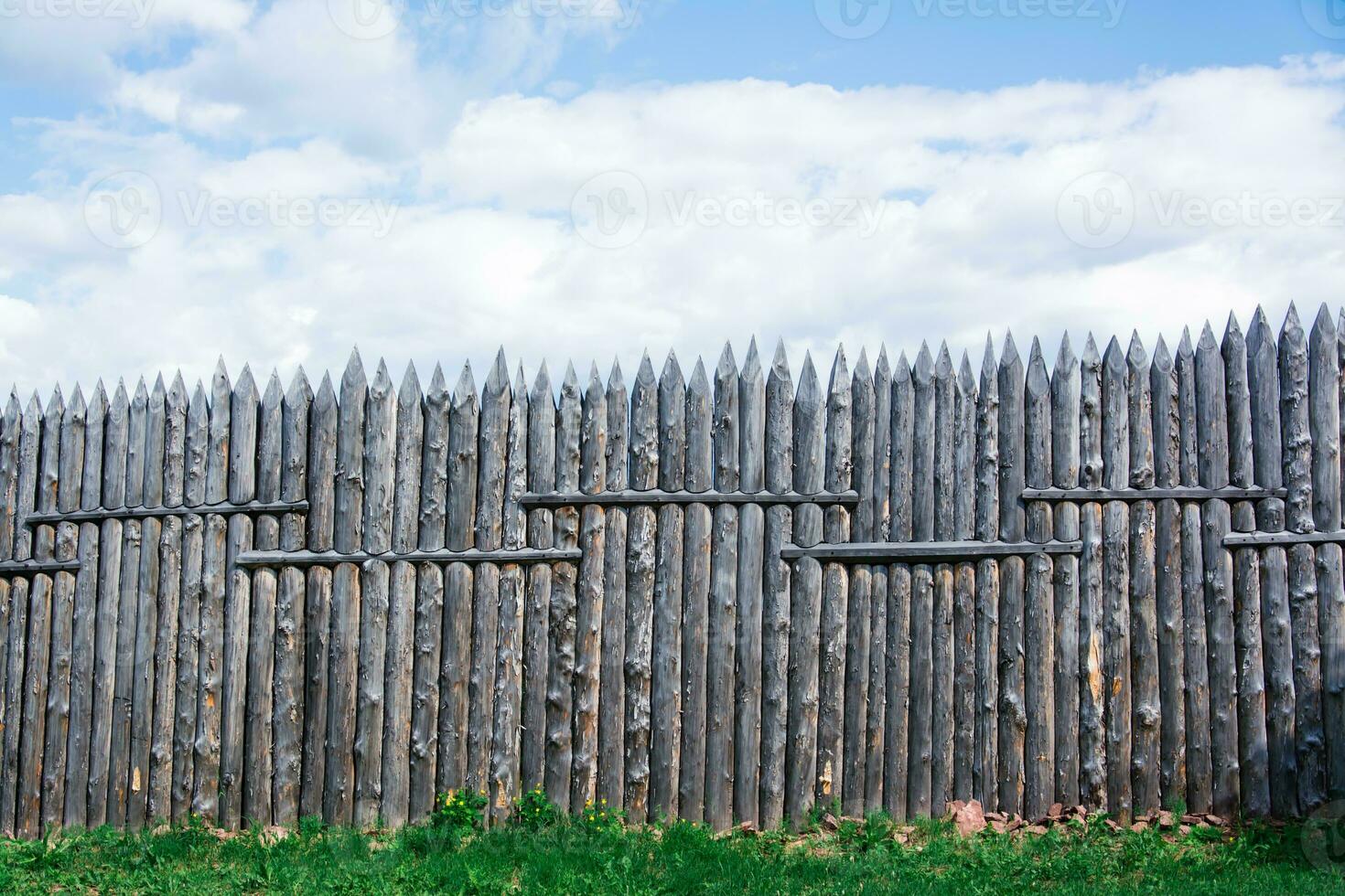 An old wooden fence made of sharp stakes in a Russian Siberian village photo