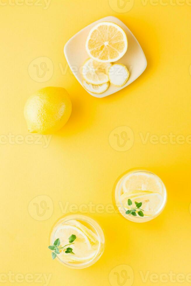Sparkling water with lemon, melissa and ice in glasses and lemon slices on a saucer on a yellow background. Alcoholic drink hard seltzer. Vertical and top view photo