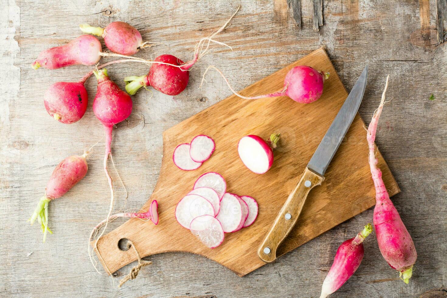 Fresh chopped radishes and a knife on a cutting board on a wooden table. Vegetables for a vegetarian diet. Rustic style. Top view photo