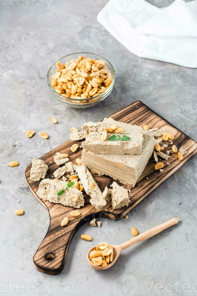 Pieces of sunflower and peanut halva and mint leaves on a cutting board and a bowl of nuts on the table. Caloric oriental dessert. Vertical view photo