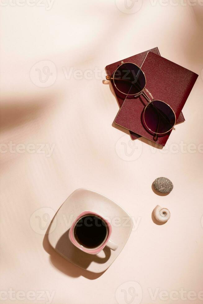 Preparing for the trip. Passports, sunglasses, seashells and a cup of coffee on a pink background in the shadows from tree leaves. Local tourism. Top and vertical view photo