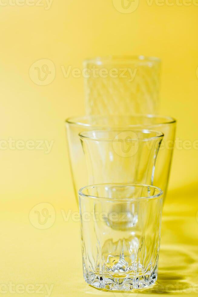 Several empty glasses of different shapes in a row in a yellow-gray palette. Inclusiveness concept. Vertical view photo