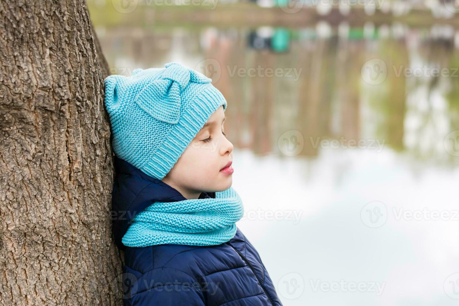 A lonely sad girl stands with closed eyes by a tree on the shore of the lake. Mental health. Teenage years photo