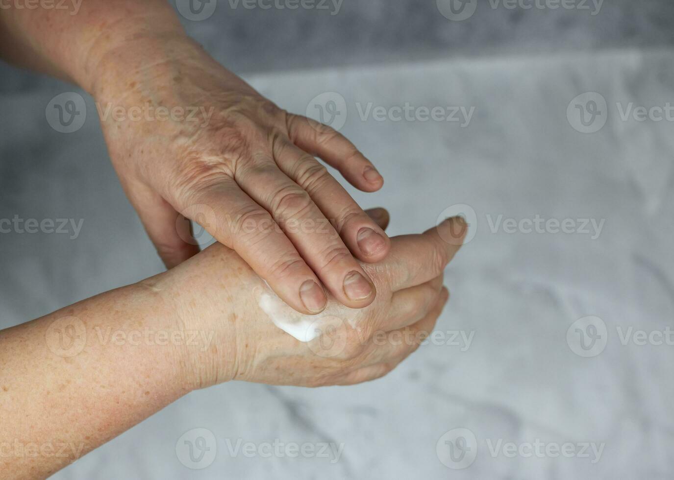 An old, elderly woman smears her hands with cream. Background and texture photo