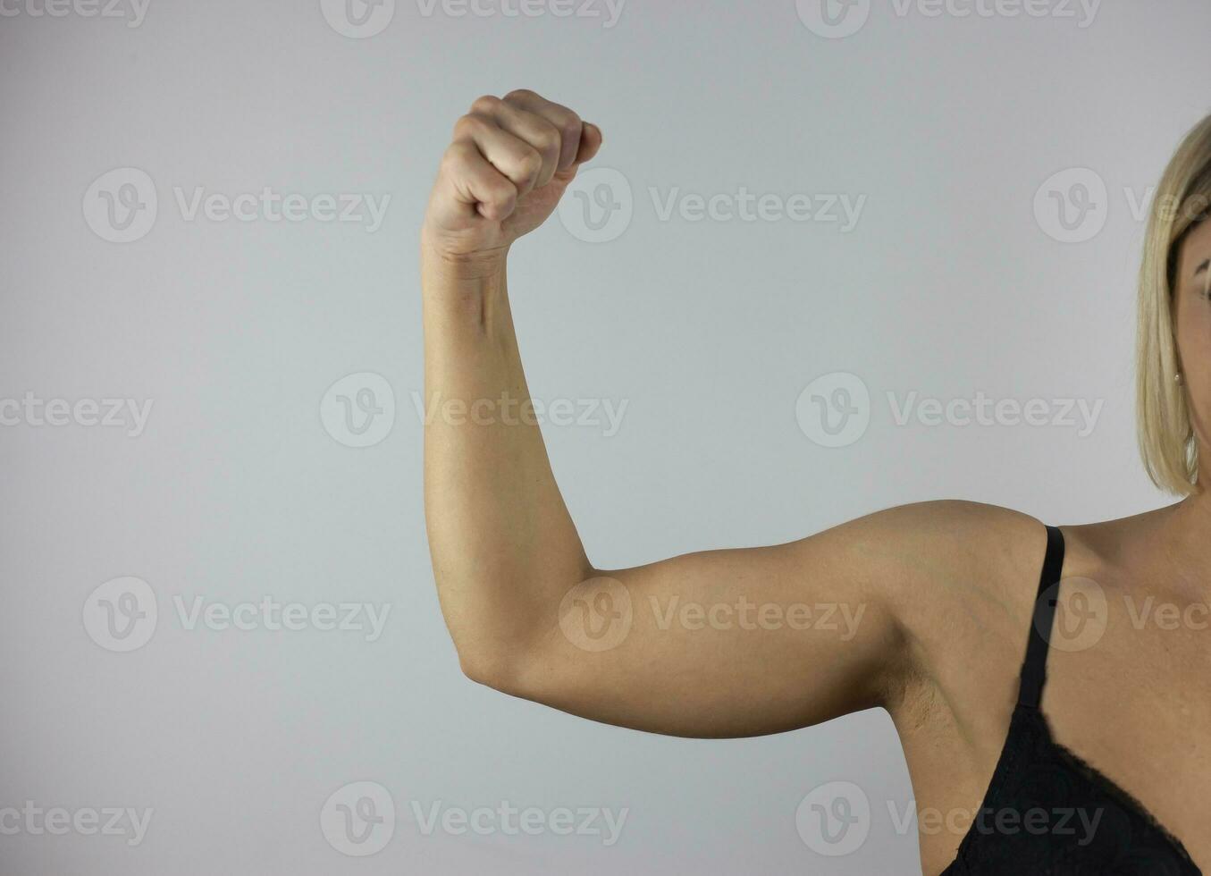 recortado Disparo de joven bronceado fuerte ajuste mujer levantamiento brazo y demostración bíceps en un blanco antecedentes. feminismo, niña fuerza, igual De las mujeres derechos, independencia, Deportes concepto. foto